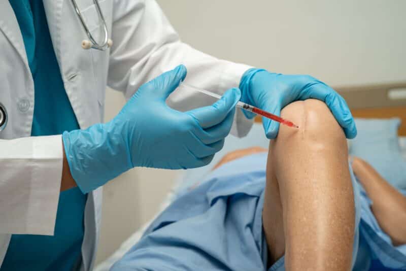 Doctor holding a syringe to administer a targeted regenerative therapy injection into a patient's painful knee joint