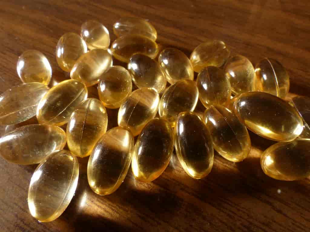 Golden liquid Vitamin D softgel capsules spilling out of a amber glass bottle onto a clean background.
